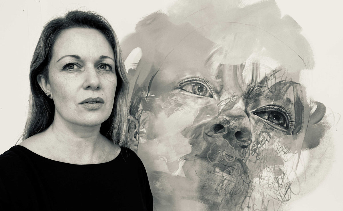 black and white photo of female artist in front of large unfinished artwork of a face 